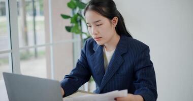 Portrait of Asian businesswoman in suit use laptop for work and analyze documents in small coffee shop. Work from anywhere, Remote working photo