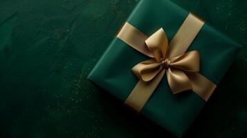 Dark green gift box with elegant gold ribbon on dark background. photo