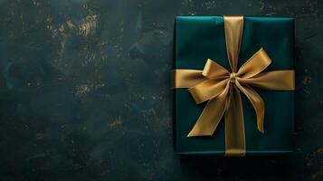 Dark green gift box with elegant gold ribbon on dark background. photo
