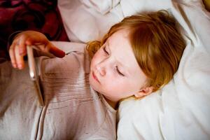 Little girl lying in bed with a thermometer in her mouth. photo