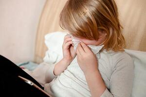 Little sick girl with a handkerchief lies in bed and cries photo