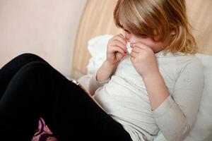 Sick little girl with a cold sneezing into a tissue photo