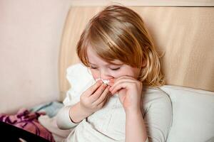 Sick little girl with flu lying in bed and blowing her nose photo