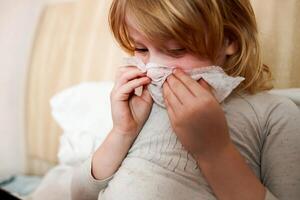 sick child with a cold sneezing in bed at home photo