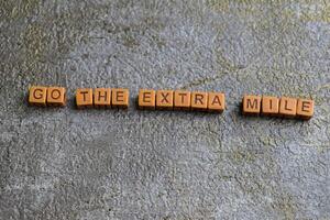 Concept of Go The Extra Mile written on wooden blocks. Cross processed image on Wooden Background photo