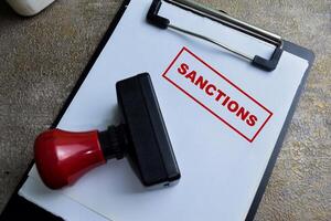 Red Handle Rubber Stamper and Sanctions text above paperwork isolated on wooden background photo