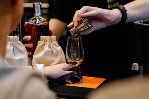 The bartender pours whiskey into a tasting glass for a sample. photo