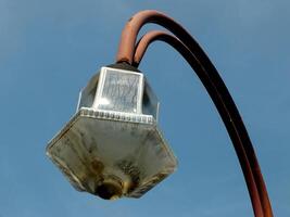 vintage outdoor street lamp with blue sky background. The lamp post is not in good condition, rusty. photo