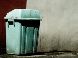 Public trash can with green color stand alone on a city street with dirty wall background. The trash can is on the side of whole image lay out. Copy space for text ads photo