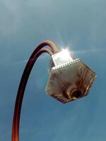 vintage outdoor street lamp with blue sky background. The lamp post is not in good condition, rusty. photo