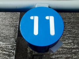 numeric number sign on blue round metal. The numeric is on white color. The object is on an outdoor area. photo