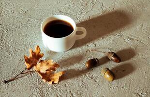 Cup of acorn coffee, acorns and autumn oak leaves on a gray background photo