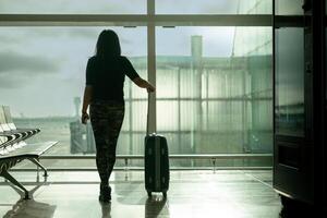Woman from behind with carry-on suitcase waiting for her flight with backlit window view photo