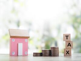 Miniature house, Wooden blocks with the word TAX and stack of coins. The concept of payment tax for house, Property investment, House mortgage, Real estate photo