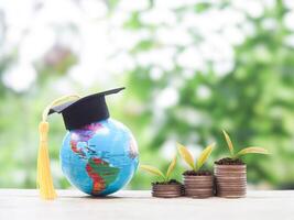 Earth globe with graduation hat and plants growing up on stack of coins. The concept of saving money for education, student loan, scholarship, tuition fees in the future photo