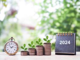Vintage watch, 2024 desk calendar and Plants growing up on stack of coins. The concept of saving money, Financial, Investment and Business growing in year 2024. photo