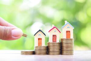 Close up hand putting coin into stack of coins and Miniature house. The concept of saving money for house, Property investment, House mortgage, Real estate photo