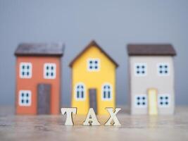 Wooden words with the TAX on stack of coins with Miniature house background. The concept of payment tax for house, Property investment, House mortgage, Real estate photo