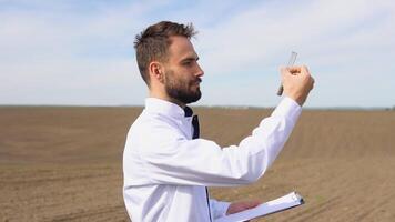 Laboratory worker holding professional glassware and testing black soil after harvest in the field video
