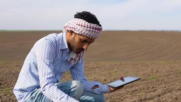Indian farmer is checking soil quality before sowing and writes the results in the tablet. Male hands touching soil on the field video