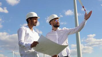 Two multiracial engineers or technician discuss about project or work using drawing paper and stand in front of cluster of windmill or wind turbine video
