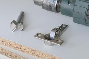 Special drill for large holes in wood. Tools for installation furniture fittings. hinge fixed on a modern cabinet. photo