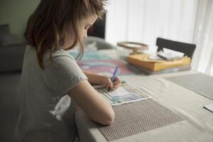 Teenage girl at home at the table solves a crossword puzzle photo