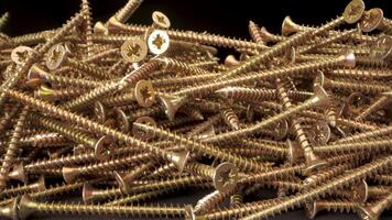 cerca arriba ver de un pila de oro tornillos. el empulgueras son arreglado en un aleatorio modelo y son iluminado por un brillante ligero. el capturas detalles de el tornillos, incluso el hilos y el cabezas video
