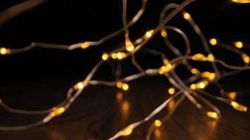 A string of copper wire lights, with small yellow bulbs, is draped across a wooden surface. The lights are on and illuminating the dark background. video