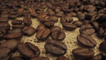 A close-up shot of roasted coffee beans scattered on a burlap surface. The beans are dark brown and shiny, with a deep, rich color. Coffee industry concept. Moving camera. video