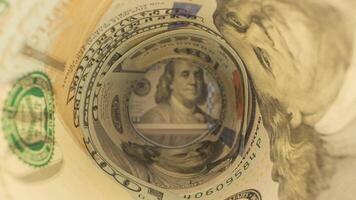 The camera pans through rolled-up hundred dollar bills. The bills are in focus, with the portrait of Benjamin Franklin prominently displayed in the center. video