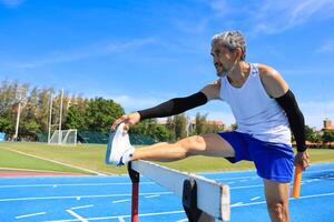 Senior Asian athlete is practicing hurdling running in the professional blue track for professional exercise, sport training workout and healthy for longevity concept photo