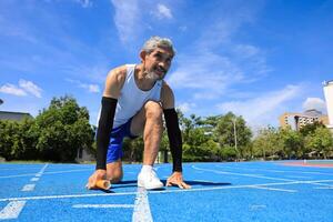 Senior Asian athlete is practicing running block start in the professional blue track for professional exercise, sport training workout and healthy for longevity concept photo