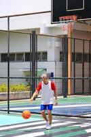 Senior Asian man in retirement age is playing basketball at outdoor court for healthy and fun activity to exercise and workout against aging illness photo
