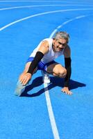 Senior Asian athlete doing stretching warm up for running in the professional blue track for professional exercise, sport training workout and healthy for longevity concept photo