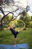 little 5-year-old gymnast in a black minimalistic leotard exercises with a hoop in the garden photo