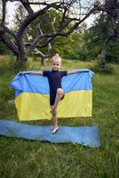 a little 5-year-old gymnast in a black minimalist jumpsuit is practicing with the flag of Ukraine in the garden photo