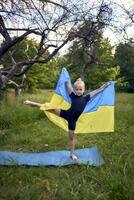 a little 5-year-old gymnast in a black minimalist jumpsuit is practicing with the flag of Ukraine in the garden photo