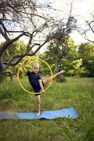 little 5-year-old gymnast in a black minimalistic leotard exercises with a hoop in the garden photo