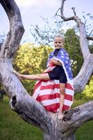a little 5-year-old gymnast in a black minimalist jumpsuit is practicing with the flag of USA in the garden photo