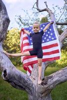 a little 5-year-old gymnast in a black minimalist jumpsuit is practicing with the flag of USA in the garden photo