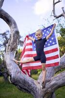 a little 5-year-old gymnast in a black minimalist jumpsuit is practicing with the flag of USA in the garden photo