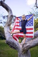 a little 5-year-old gymnast in a black minimalist jumpsuit is practicing with the flag of USA in the garden photo