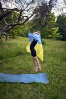 a little 5-year-old gymnast in a black minimalist jumpsuit is practicing with the flag of Ukraine in the garden photo