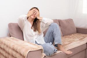 Young beautiful woman sitting on sofa and crying at home photo