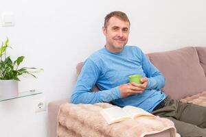 Relaxing at home, a man sits on the sofa and reads a book in front of him, enjoying a quiet moment photo