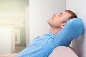 portrait of a happy man with long dark hair who dreams with closed eyes on the sofa in a bright living room. white background, space for text photo