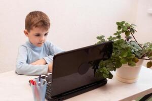 child student returns to school. boy smiles, writes or draws and reads on laptop while doing homework. teaching people at home in bedroom, studying online on computer photo