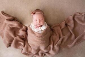 a beautiful baby in a cap sleeps on a beige background covered with a soft, fluffy blanket photo