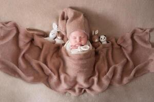 a beautiful baby in a cap sleeps on a beige background covered with a soft, fluffy blanket photo